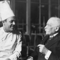 Auguste Escoffier en habit de chef, assis auprès d’un homme âgé